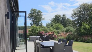 An outdoor patio with a table and chairs, a glass door leading to the interior, and a garden with trees and shrubs. - 5 Star Holiday Home in Falkenberg (Falkenberg)