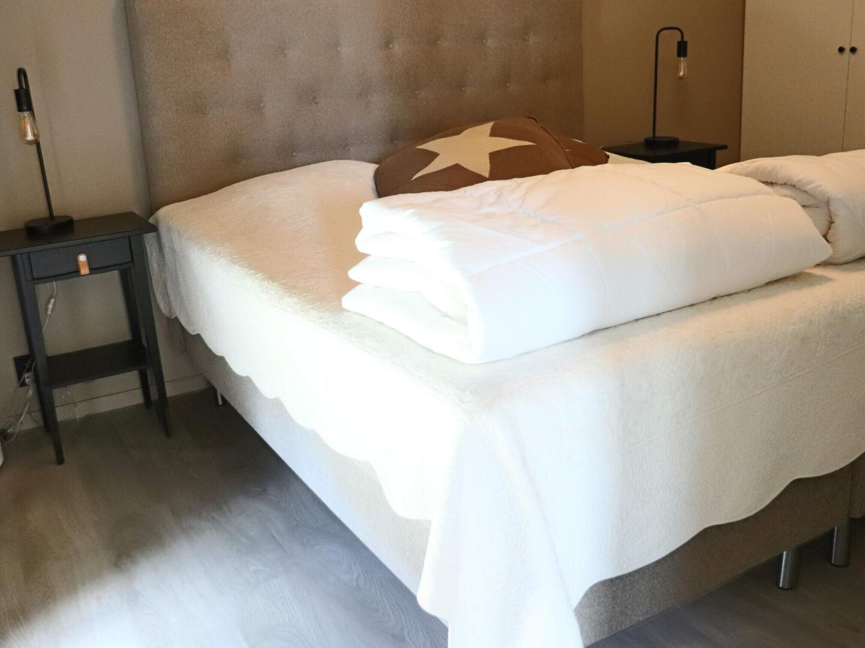 A neatly made bed with a white duvet and a brown pillow, a bedside table with a lamp, and a wardrobe in a hotel room.