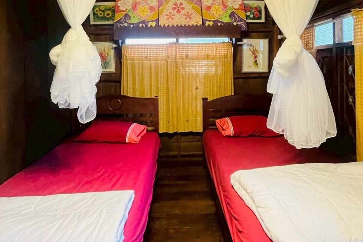 A room with two beds, a wooden floor, a curtain, and a chandelier.