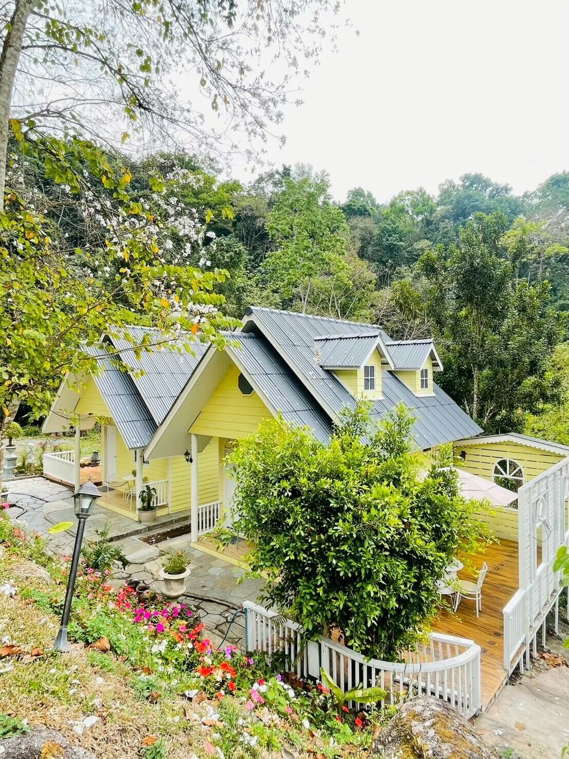 A yellow cottage with a sloped roof, surrounded by lush greenery and a small garden.