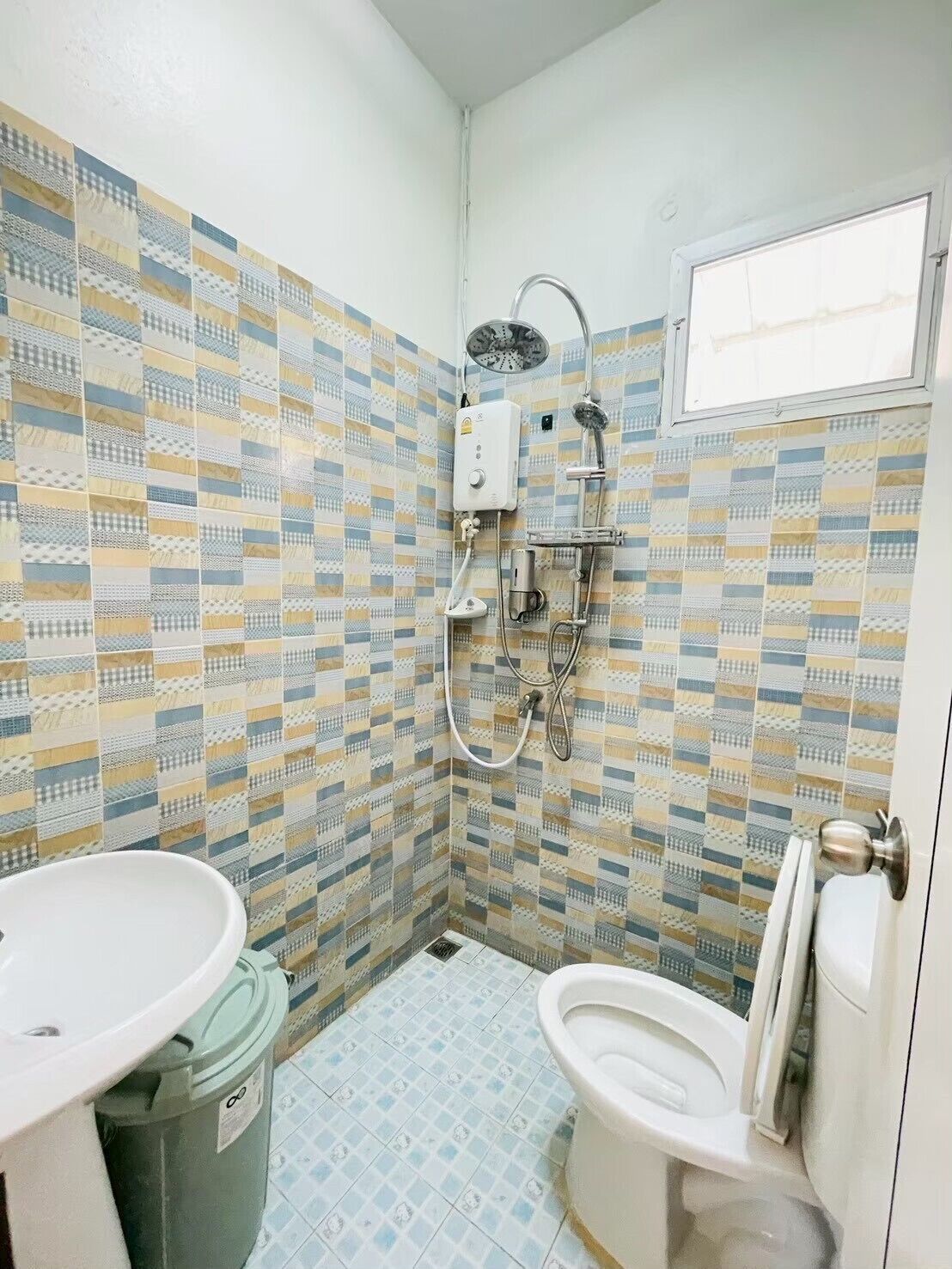 Een badkamer met een douche, toilet en wastafel, met decoratieve tegels en een witte deur.