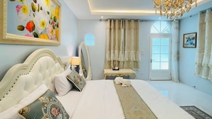 A bedroom with a large bed, a chandelier, a painting, and a window.