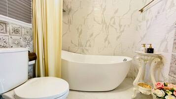 A bathroom with a freestanding bathtub, a toilet, a vanity with a mirror, and a shower curtain.