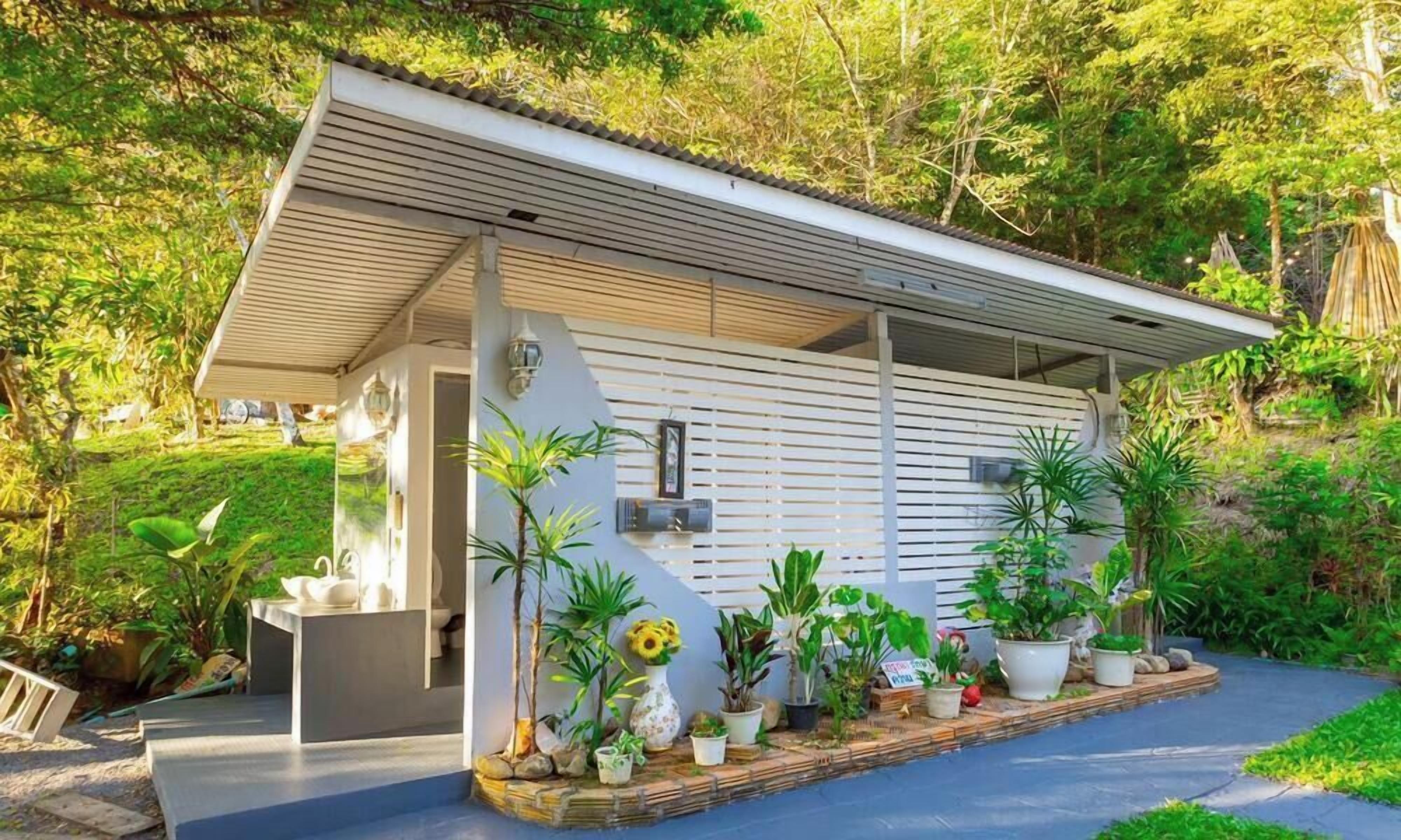 A modern house with a covered porch, surrounded by lush greenery and various potted plants.