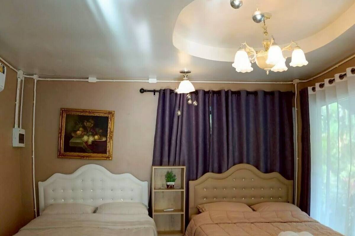 A hotel room with two beds, a chandelier, a painting, and a window with curtains.