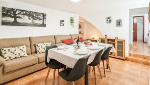 A dining area with a table set for four, a sofa with patterned cushions, and a painting on the wall.
