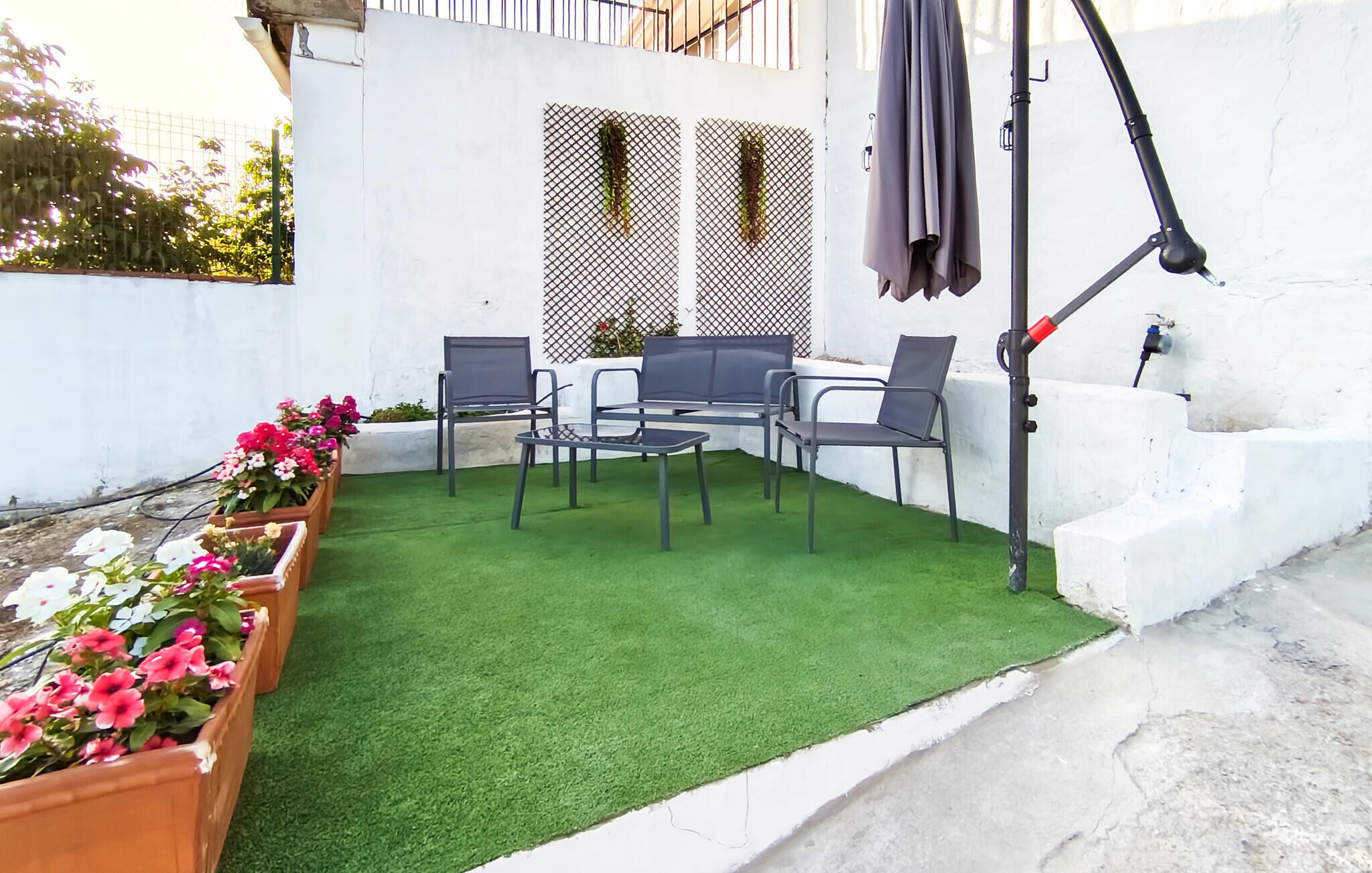 A patio with artificial grass, a table, four chairs, and potted plants.