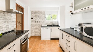 A modern kitchen with a brick wall backsplash, white cabinetry, and a window.