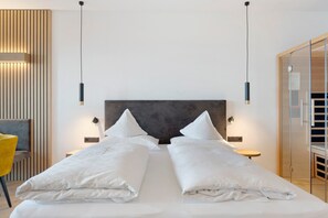 Ein Hotelzimmer mit einem großen Bett, Nachttischen, einem Sessel und einer Glastür zu einem Badezimmer.