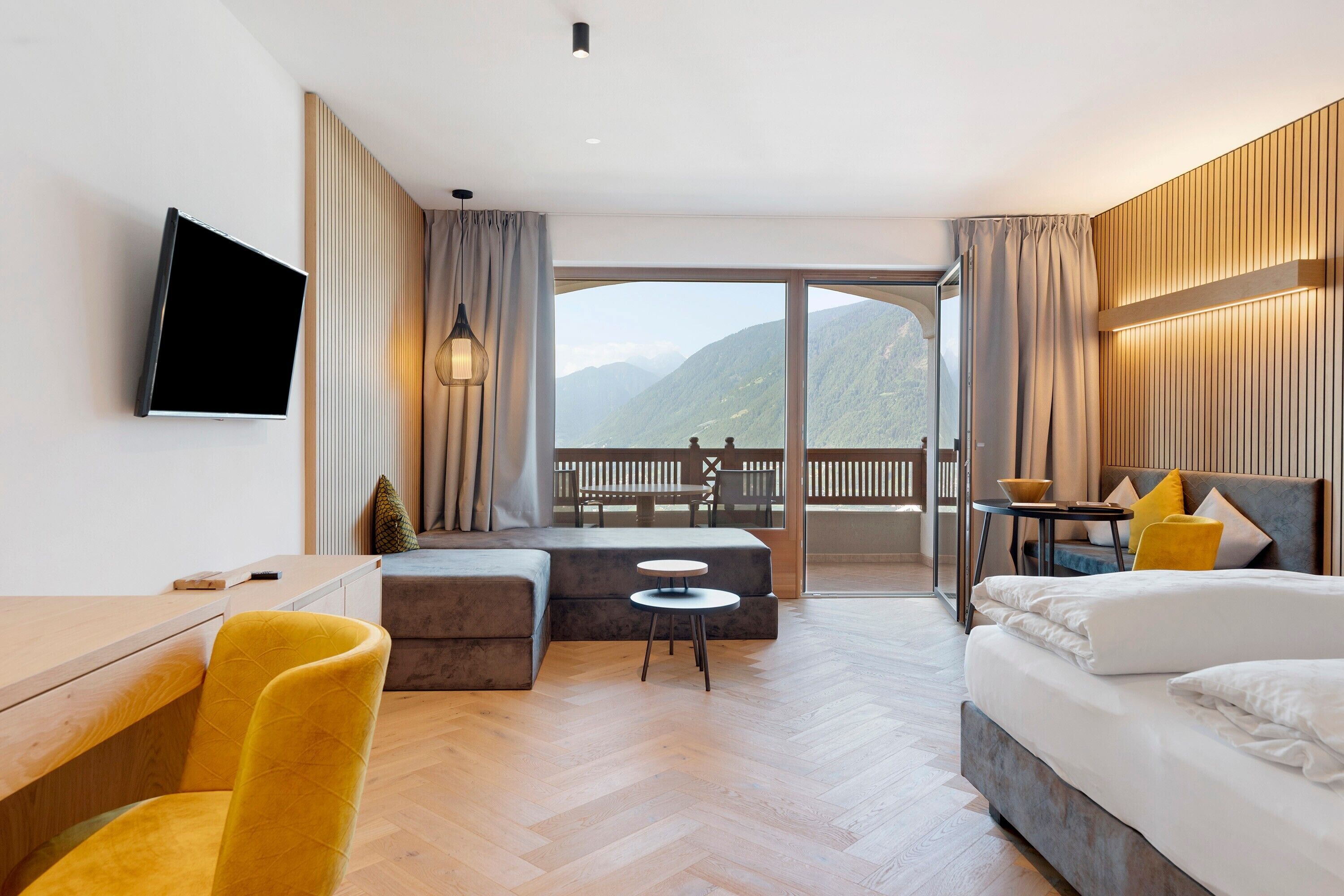 Een hotelkamer met een bed, een bureau, een bank en een balkon met uitzicht op bergen.