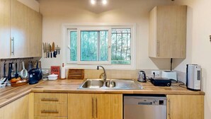 Una cocina con armarios de madera, un lavamanos doble, una ventana con vistas a árboles y un lavavajillas.