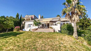 Una casa de dos pisos con un balcón, un patio techado y una palmera.