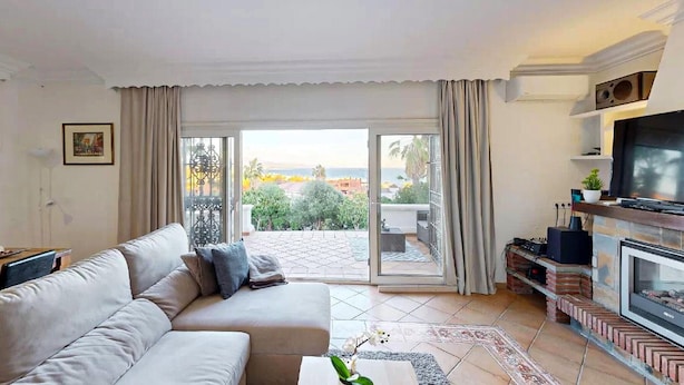 Una sala de estar con sofá, televisión, chimenea y vistas a zonas verdes y edificios.