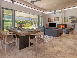 A modern living room with a fireplace, large windows, and a dining area.