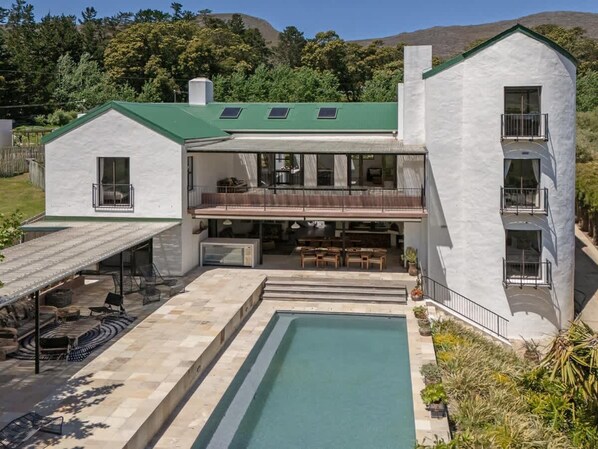 A two-story house with a pool, outdoor seating, and a green roof.