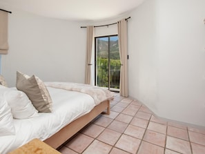 A bedroom with a bed, curtains, and a view of greenery through a sliding door.