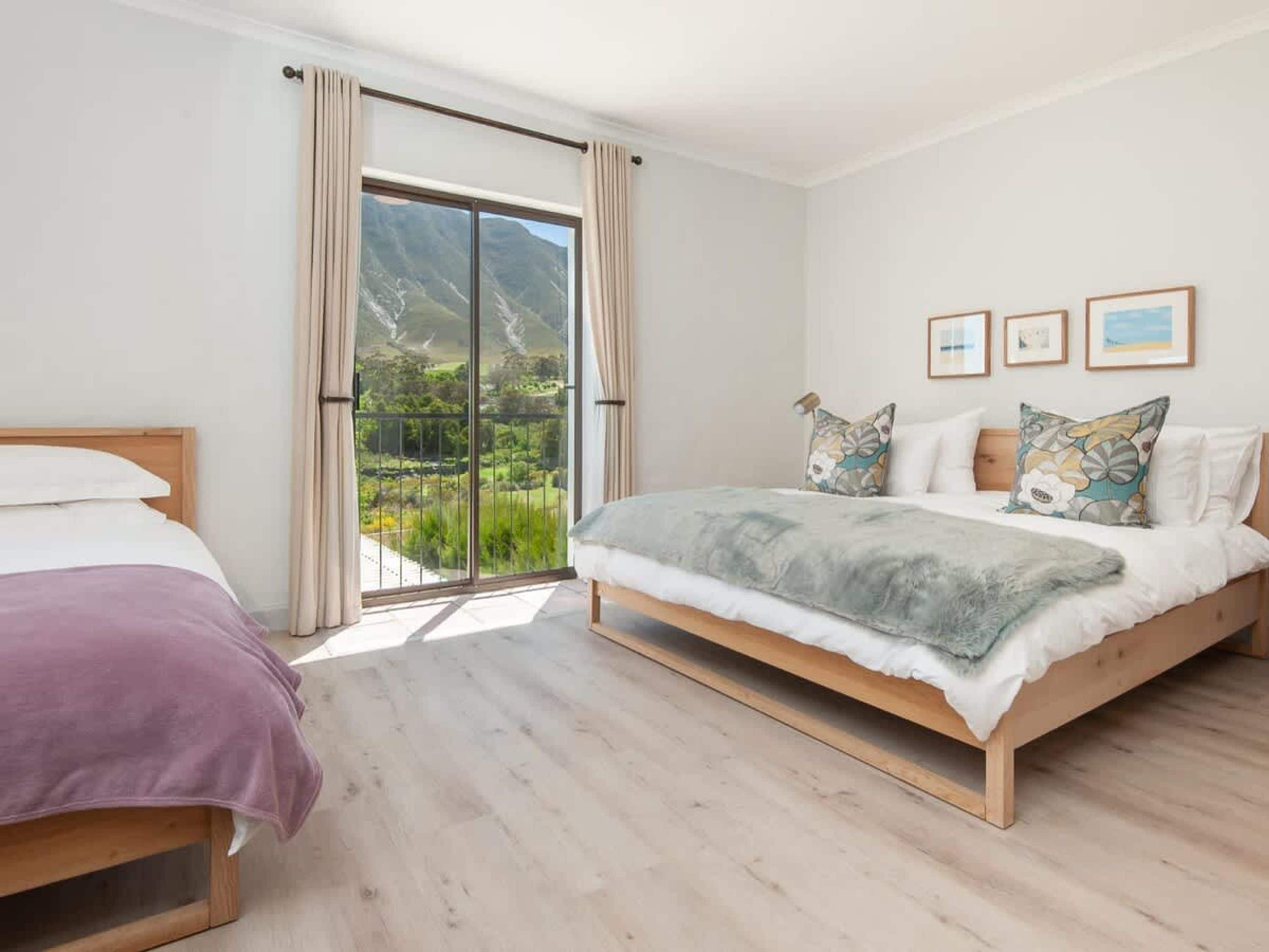 A bedroom with a large sliding glass door to a balcony, a bed with a grey blanket, and three framed pictures on the wall.