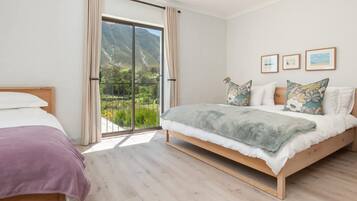 A bedroom with a large sliding glass door to a balcony, a bed with a grey blanket, and three framed pictures on the wall.
