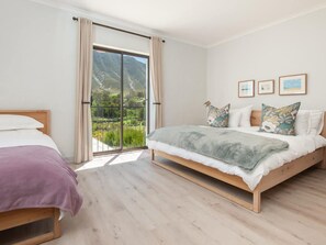 A bedroom with a large sliding glass door to a balcony, a bed with a grey blanket, and three framed pictures on the wall.