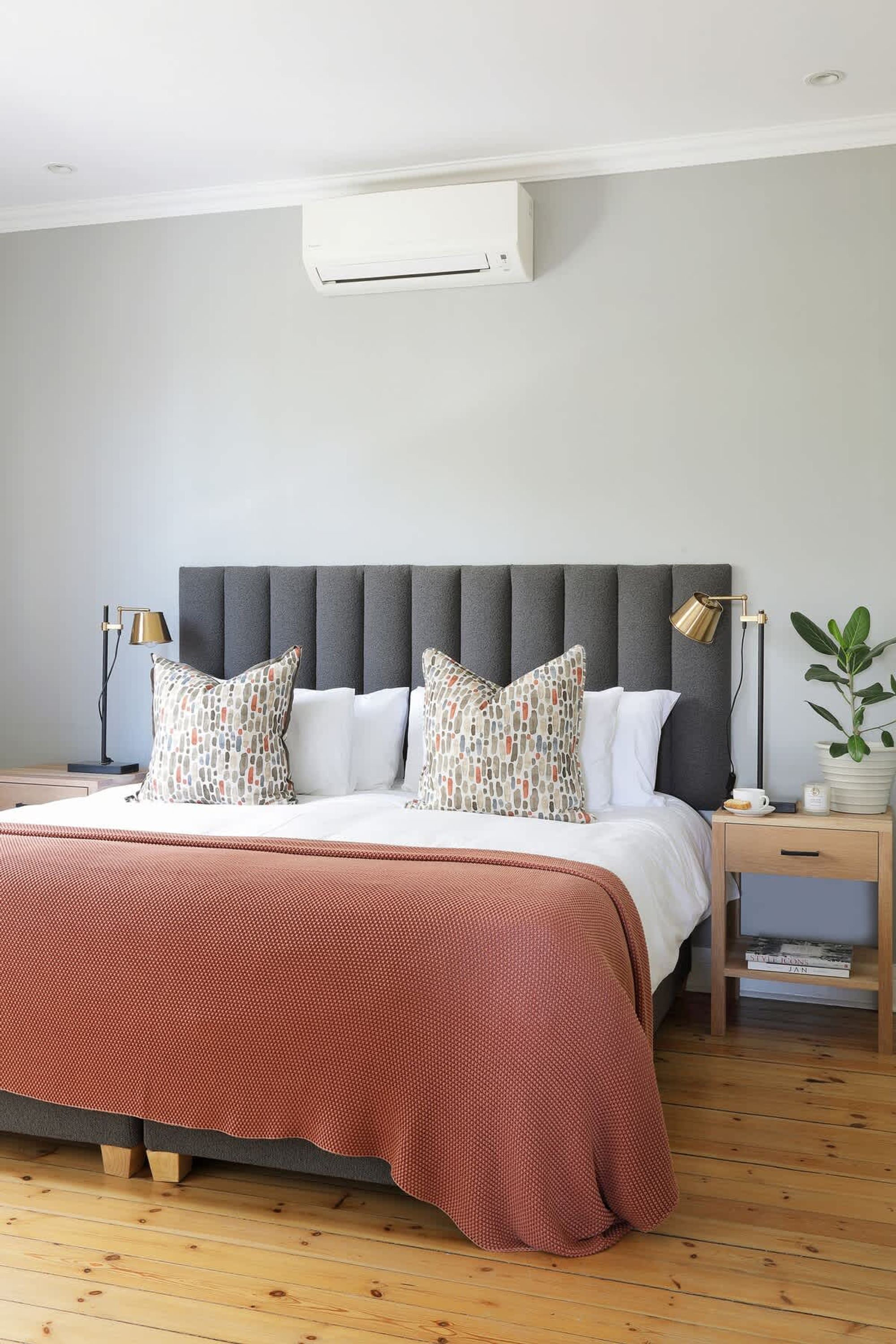 Un dormitorio con cama, mesitas de noche, lámpara, planta en maceta y aire acondicionado instalado en la pared.