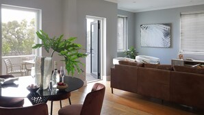Uma sala de estar moderna com um sofá marrom, uma mesa de jantar com cadeiras, uma planta grande e uma porta de vidro que dá para o exterior.