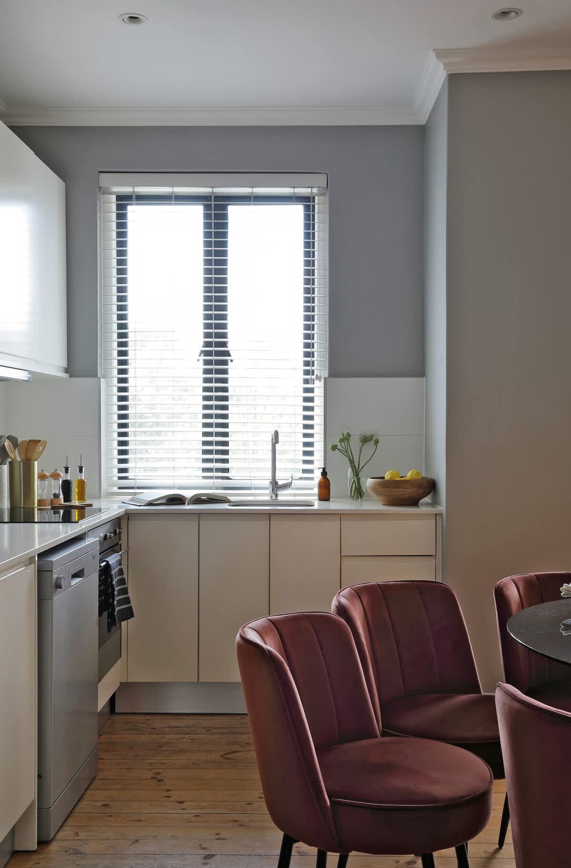 A modern kitchen with a window, a sink, and a dining area with chairs.