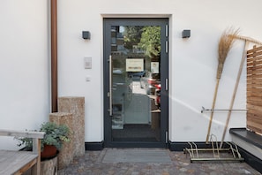 Ein moderner Eingangsbereich mit Glastür, einer Holzbank, einem Blumentopf und einer Metallbank.