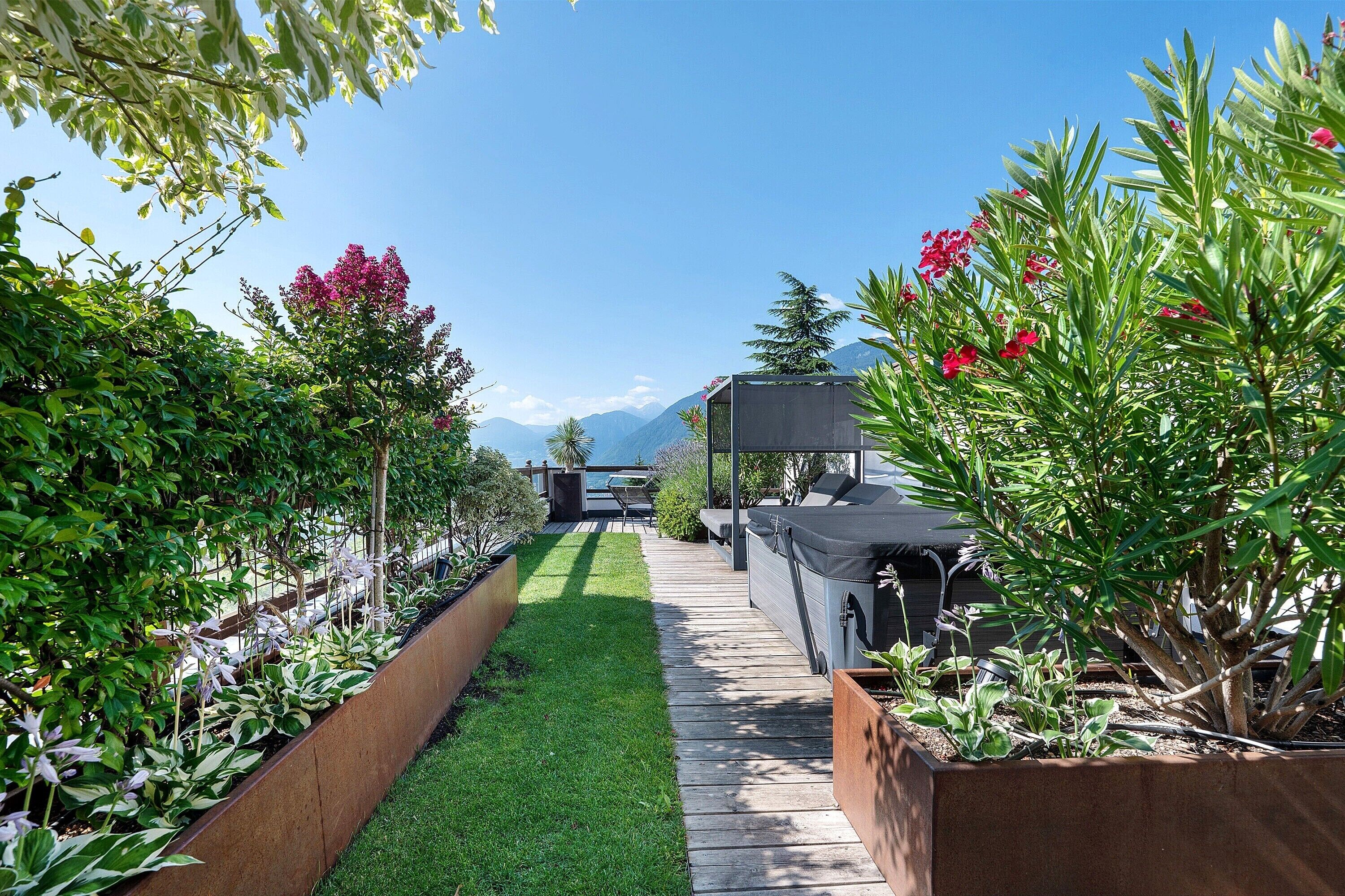 Un sentier de jardin mène à un espace aménagé avec un coin salon et un barbecue, le tout entouré de différentes plantes et arbres.