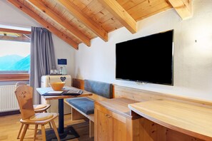 Ein Holzinterieur mit Esstisch, Stühlen, einer Bank, einem Fernseher und Blick auf Berge.
