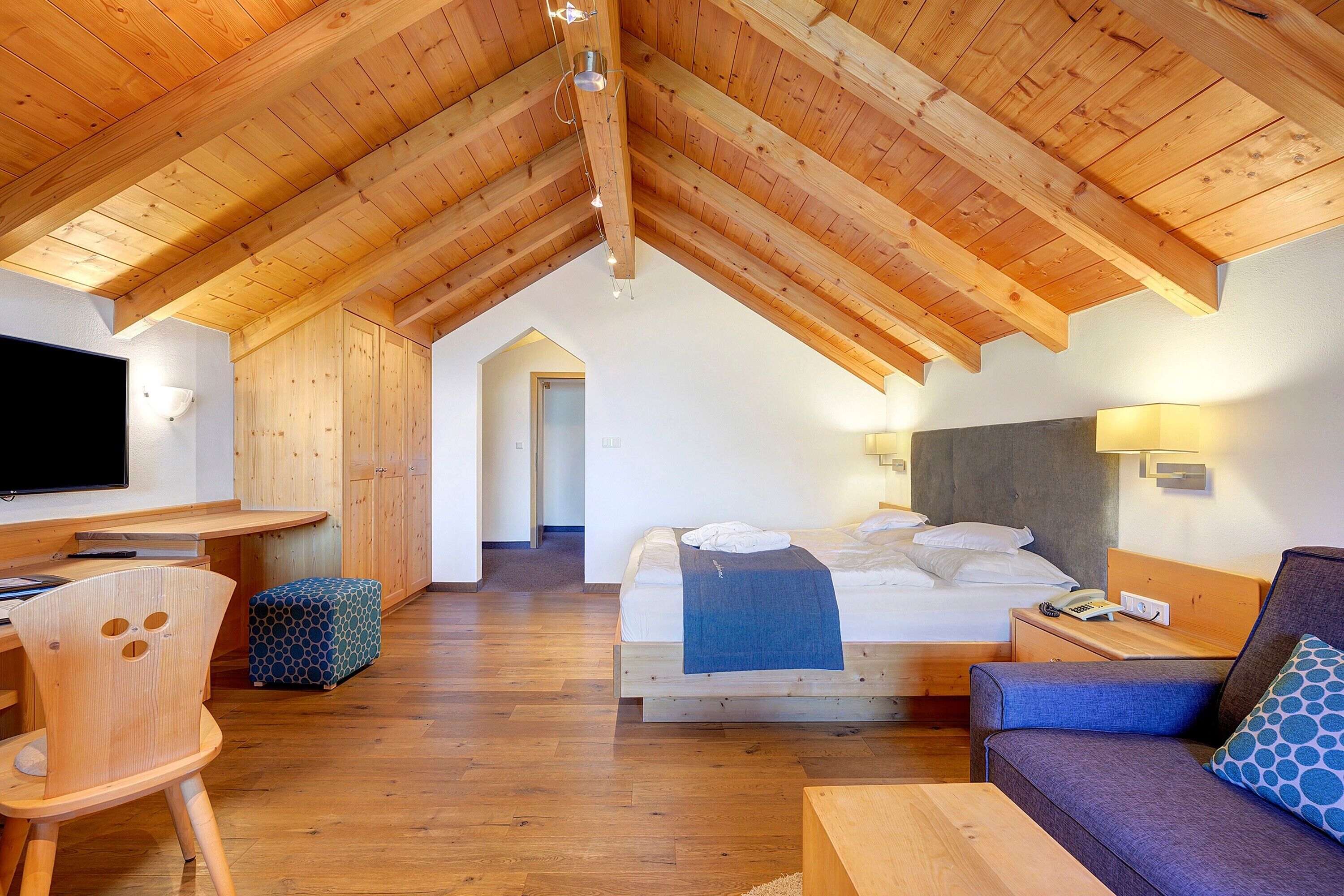 Ein Zimmer mit Holzboden, einem Bett, einem Schreibtisch mit Computer, einem Sessel und einer Couch.