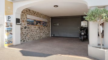 Entrada de hotel con un muro de piedra, una puerta de garaje cerrada y una motocicleta estacionada afuera.