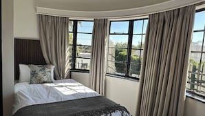 A bedroom with a bed, curtains, and a view of the outside. - Room-rosarios Village 11 Taplow (Johannesburg)