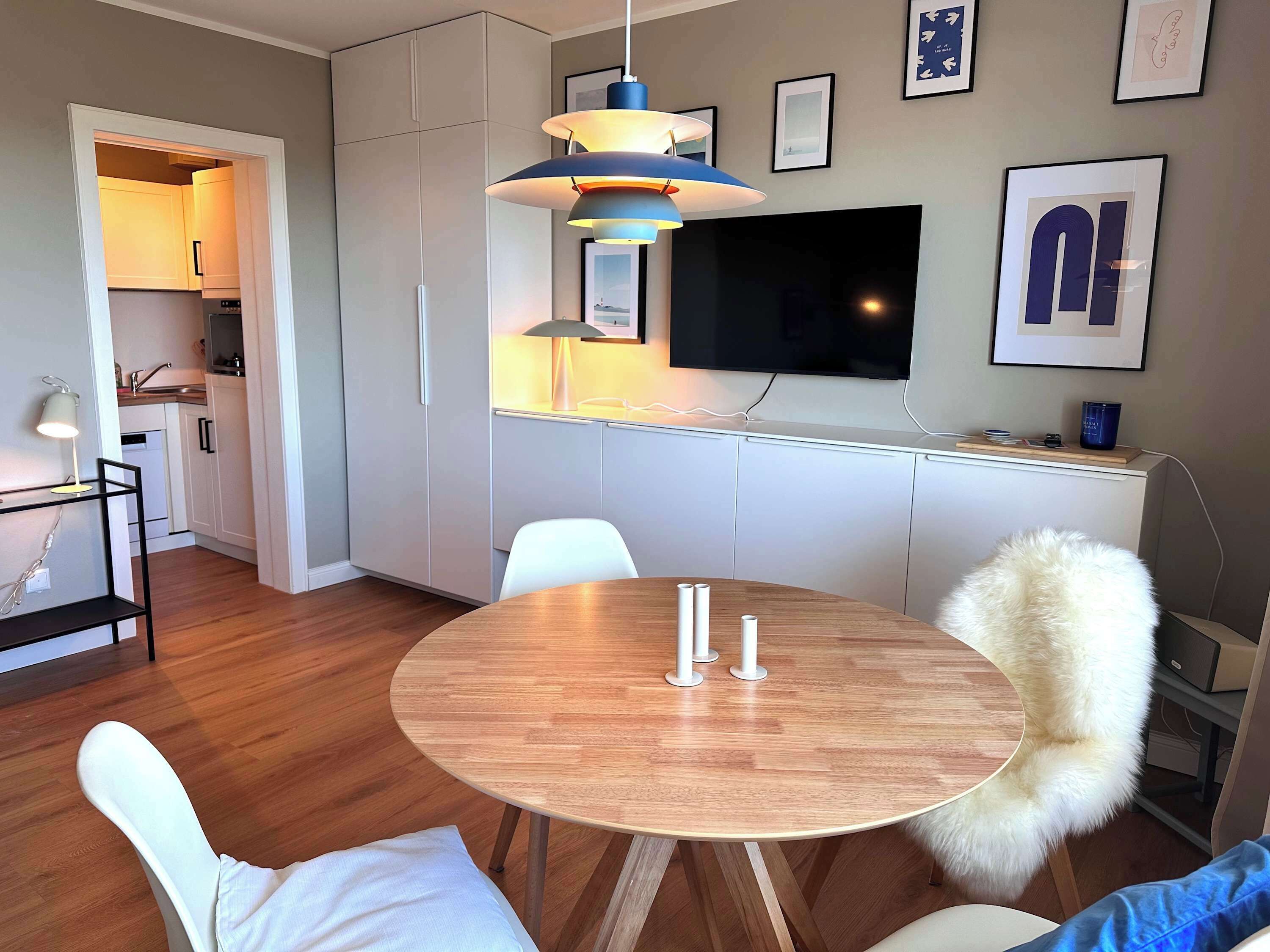 A modern kitchen with white cabinets, a dining area with a round wooden table, white chairs, and a fluffy white chair.