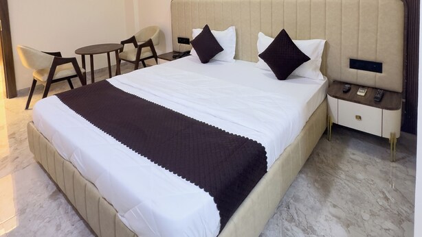 A hotel room with a large bed, a bedside table with a phone, a chair, a small table, and a ceiling fan. - Hotel White Desert (Bhuj)