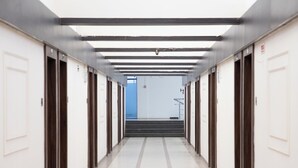 A long, narrow hallway with doors on both sides, leading to a staircase at the end. - Hotel White Desert (Bhuj)