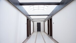 A long, narrow hallway with a skylight ceiling, white walls, and a central door. - Hotel White Desert (Bhuj)