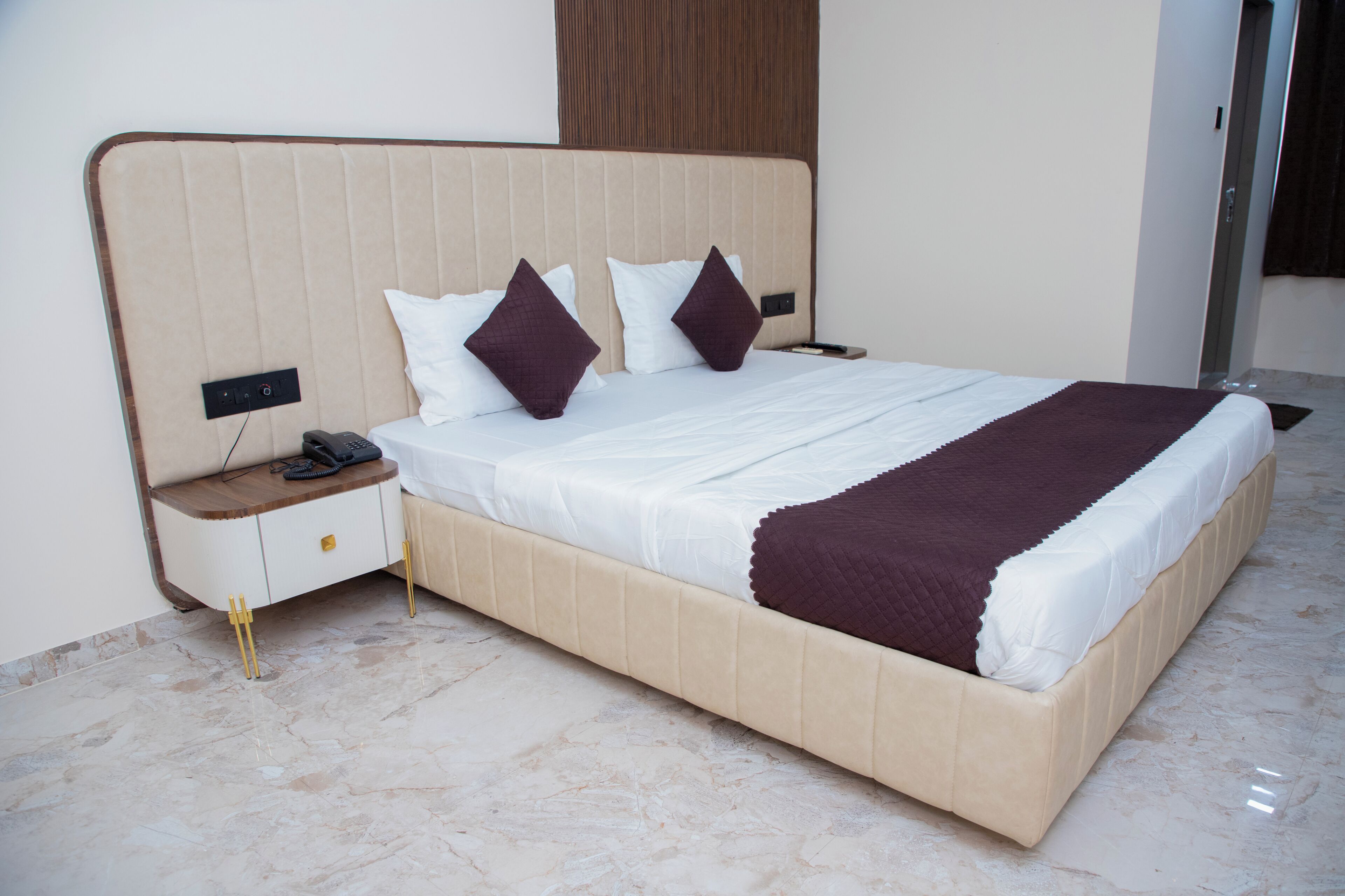 Una cama bien hecha con cabecera, una mesita de noche con un teléfono y un mueble con cajones.