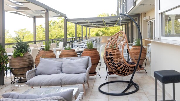 Un patio exterior con zona de estar cubierta, que incluye un sofá, sillas y una mecedora colgante.