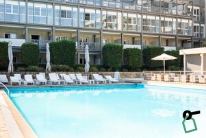 Una piscina al aire libre, sombrillas, sillones reclinables de piscina