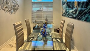 Ein Esszimmer mit einem Glastisch, Metallstühlen, einer Chandelier und einem großen abstrakten Gemälde an der Wand.