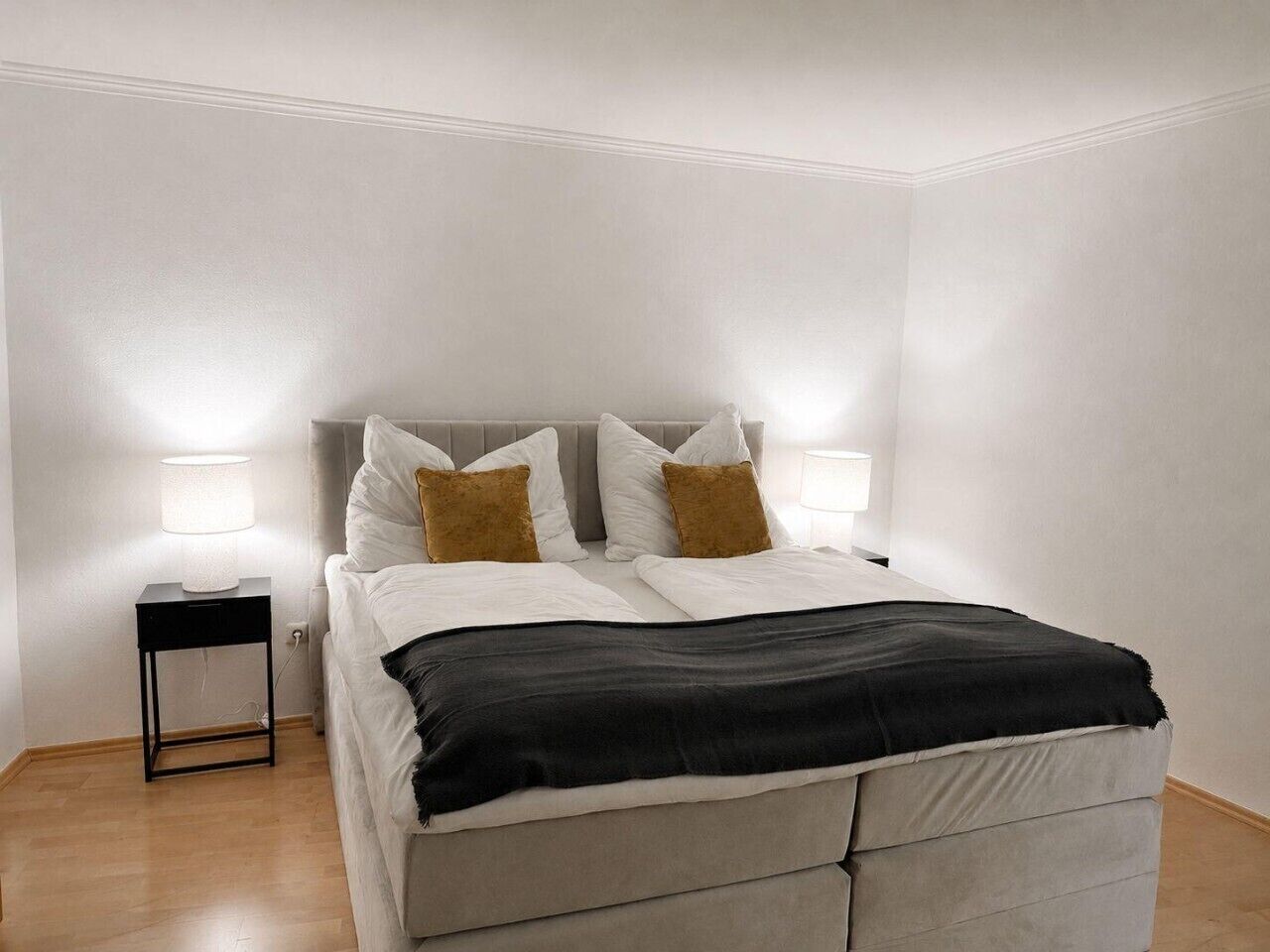 Een slaapkamer met een bed, bedlampen, een nachtkastje en een houten vloer.