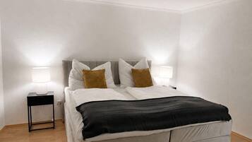 Een slaapkamer met een bed, bedlampen, een nachtkastje en een houten vloer.