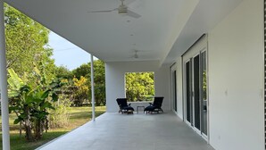 Ein überdachter Außenbereich mit Tisch und Stühlen, einem Deckenventilator und Blick auf Grünflächen.