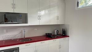 Eine Küche mit weißen Schränken, einer roten Arbeitsplatte, einer Mikrowelle, einem Wasserkocher und einer Kaffeemaschine.
