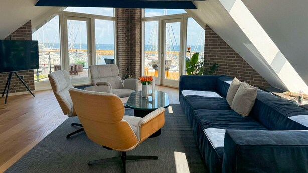 Una habitación moderna estilo loft con un ventanal grande, un televisor de pantalla plana, un sofá, una mesa de centro y una silla.