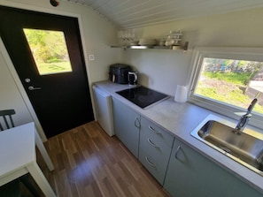 A compact kitchenette with a built-in stove, a coffee maker, and a window overlooking a garden. - 3 Person Holiday Home in Onsala (Gottskar)
