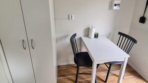Un petit coin repas avec une table blanche et deux chaises, une prise de courant et un climatiseur fixé au mur.