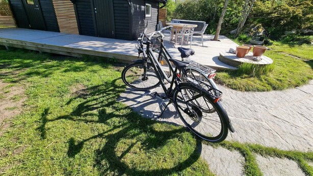 Un bâtiment en bois doté d’un porche couvert, un vélo garé sur la pelouse et du mobilier d’extérieur.