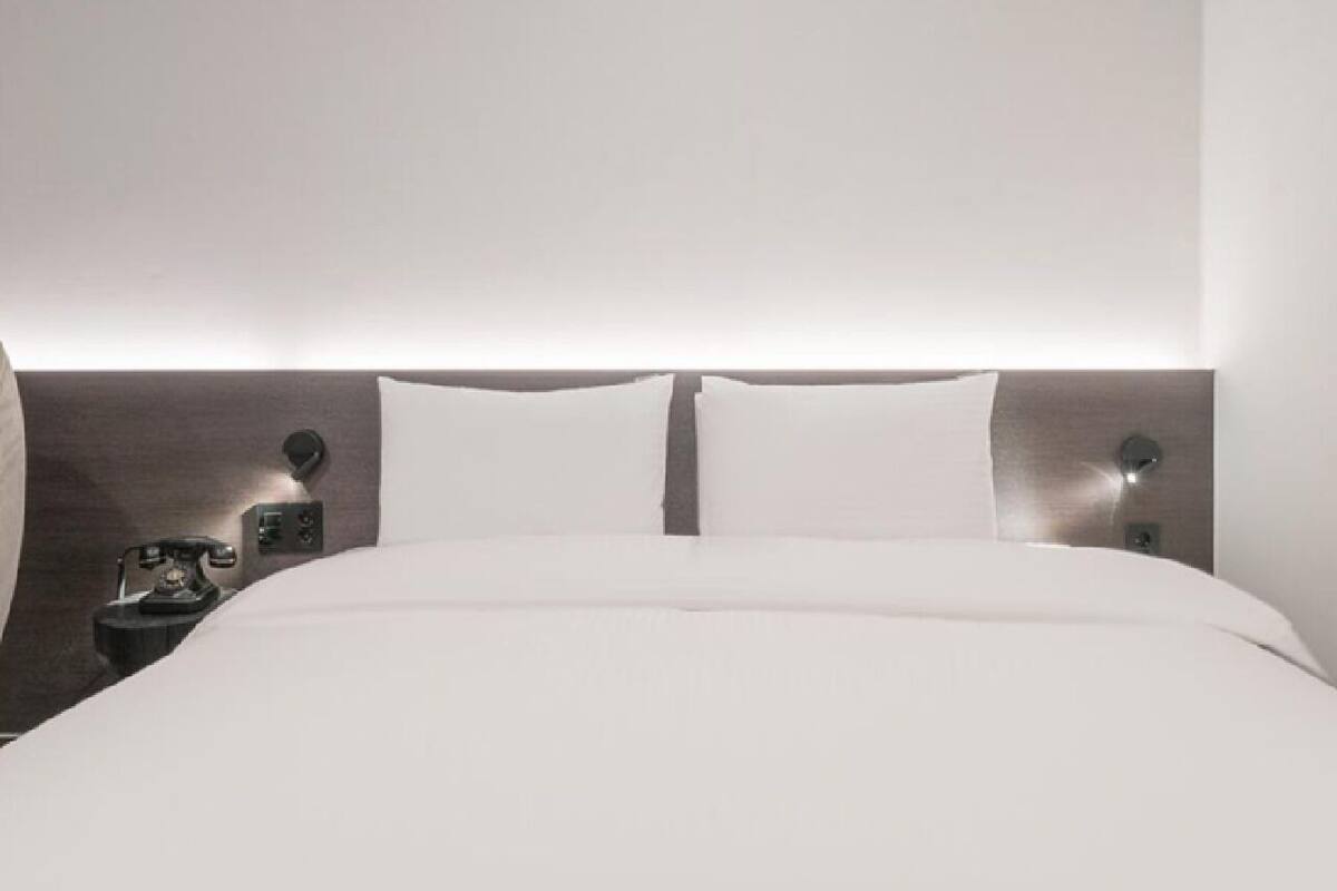 A modern hotel room with a large bed, a bedside telephone, and a wall-mounted light fixture.