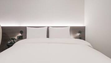 A modern hotel room with a large bed, a bedside telephone, and a wall-mounted light fixture.